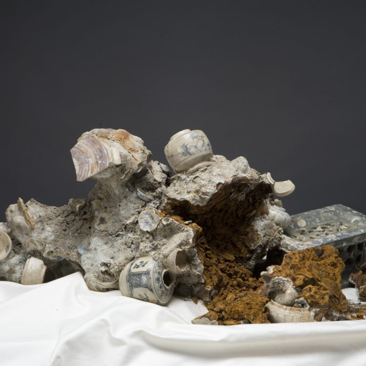 A concretion of sea matter and ceramics arranged on a white sheet.
