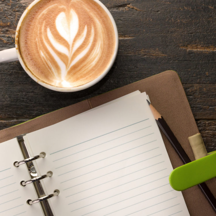 Open blank notebook beside a cup of coffee.
