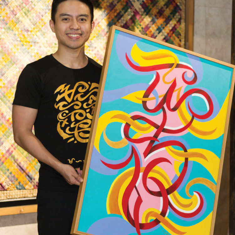 A smiling young man holds a 2 x 4' painting of a stylized script. The background is turquoise blue and the script is in pink, yello, red, and purple swirls.