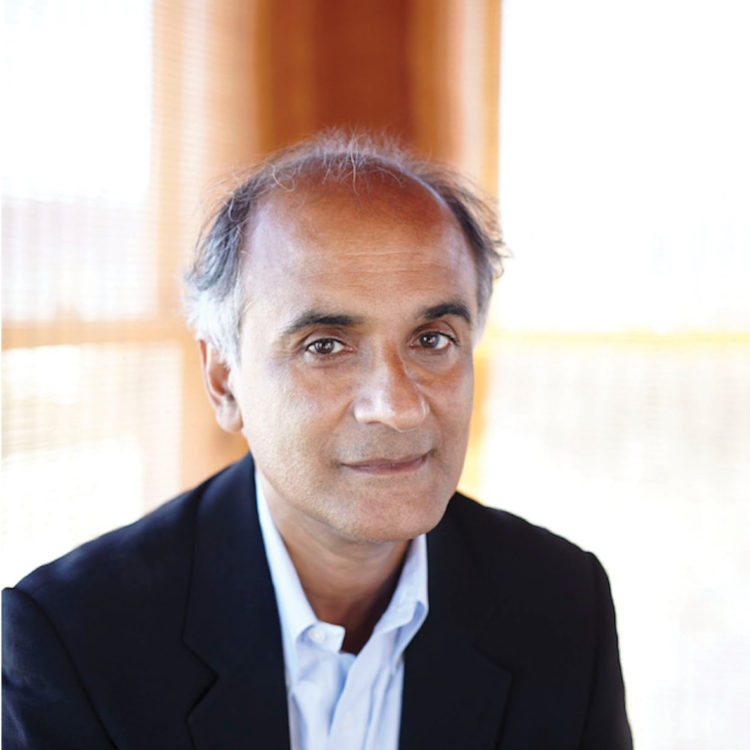 portrait of a man sitting in front of a window. he is balding and wears a dark blue blazer and white button down shirt.