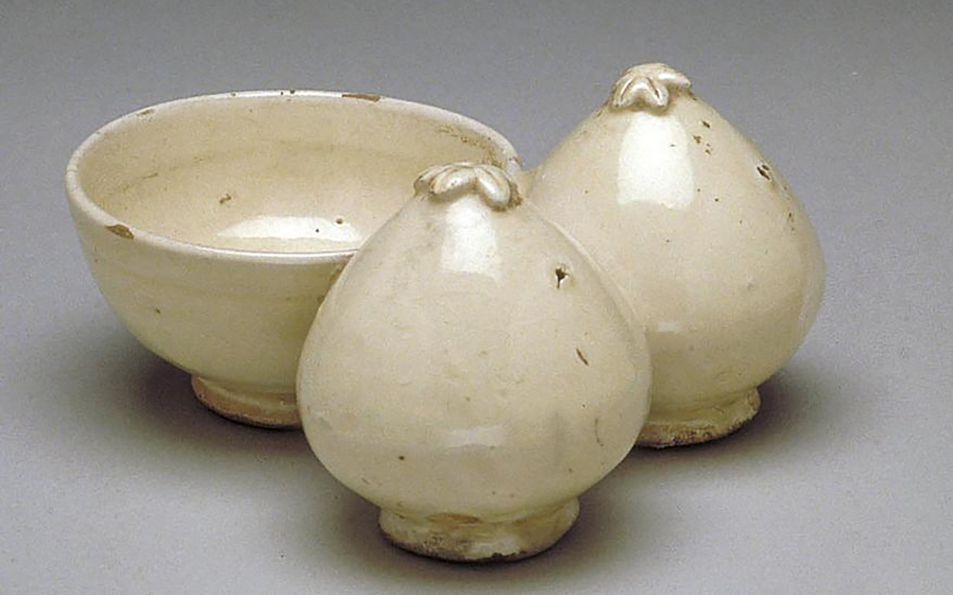 Cream colored ceramic bowl attached to two persimmon-like shapes.
