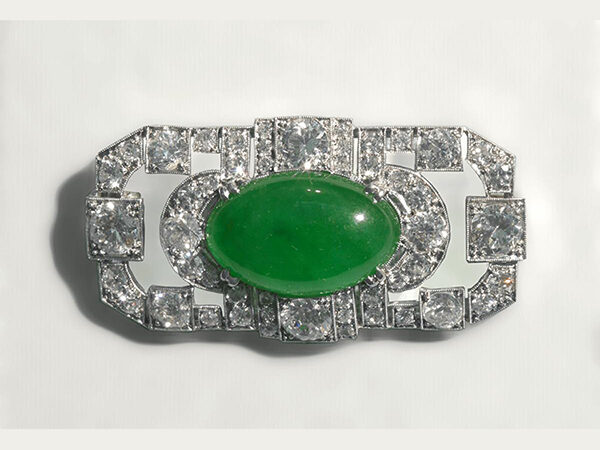 Oblong green stone set in a diamond studded silver brooch.