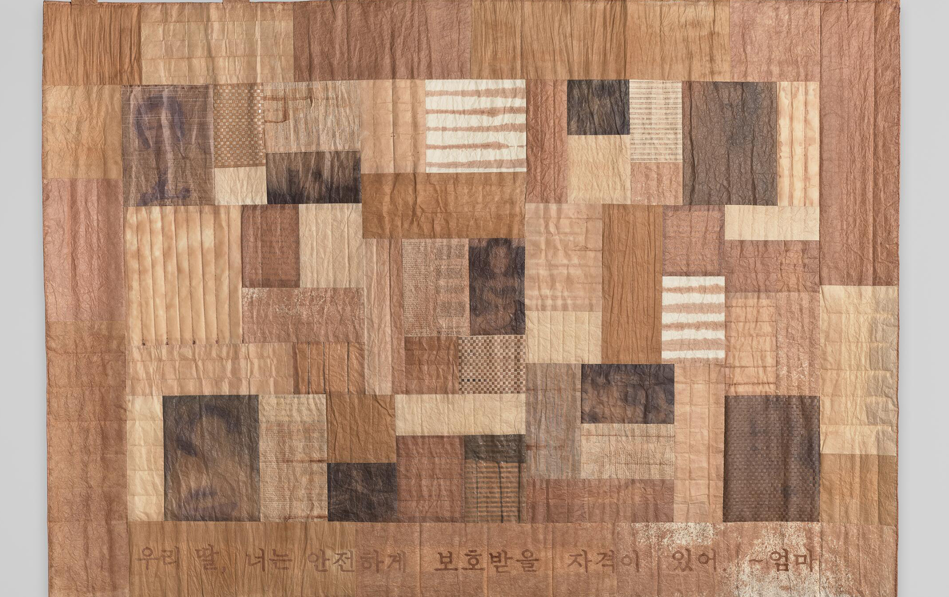 Patchwork artwork made of various shades of brown paper stitched together.