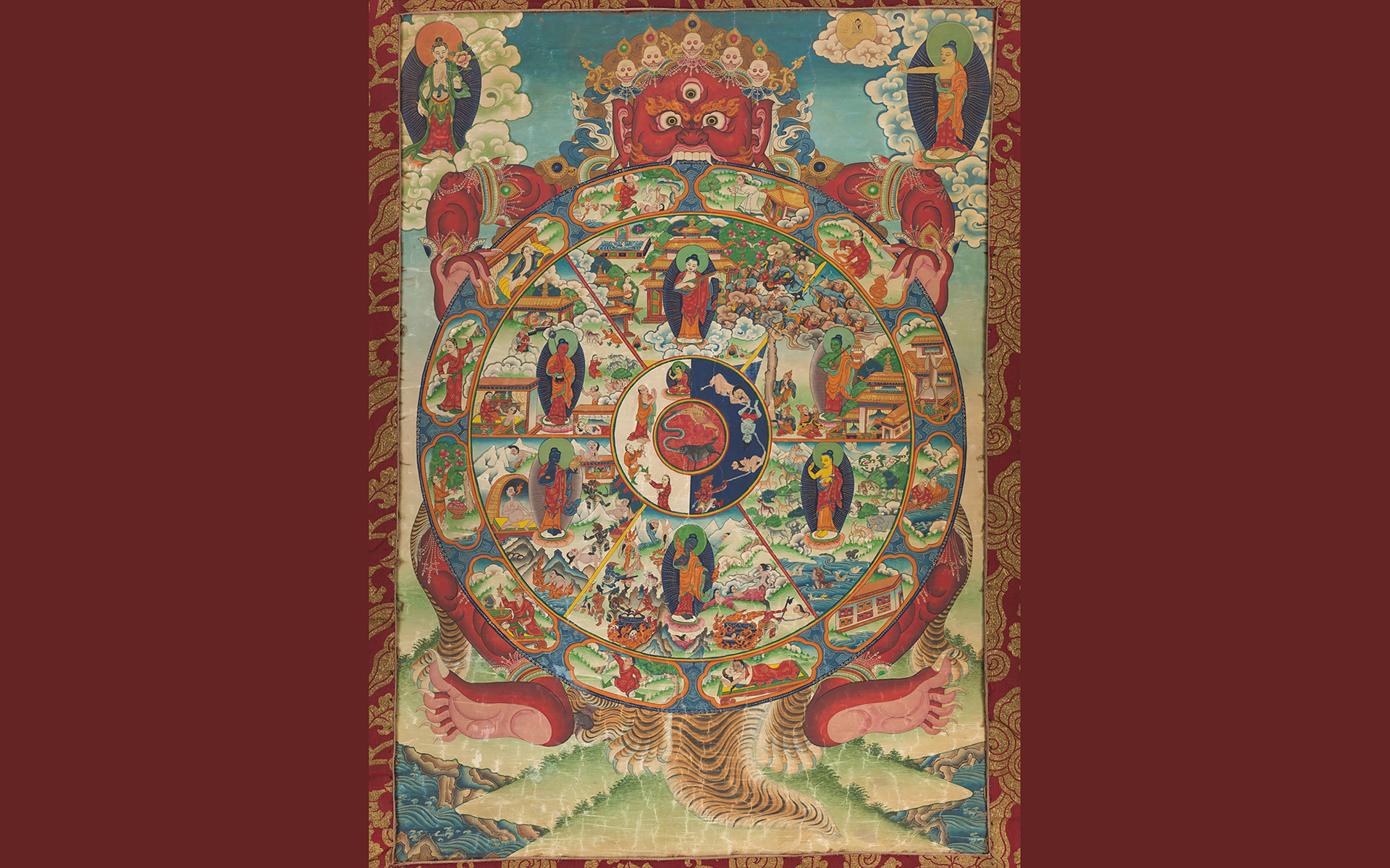 Painting of a red monster holding a wheel-shaped diagram with images of animals, gods and humans in different realms.