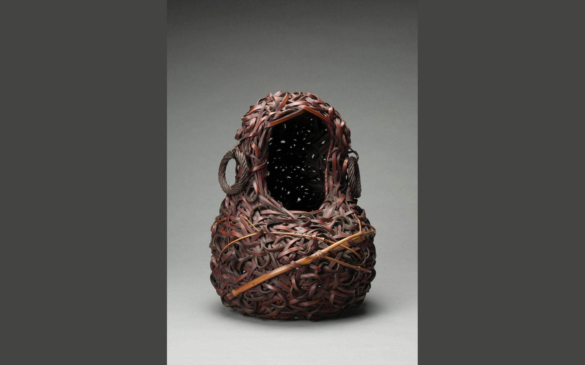 Hourglass silhouette-shaped bamboo basket evoking the image of a seated monk with large hoop earrings.